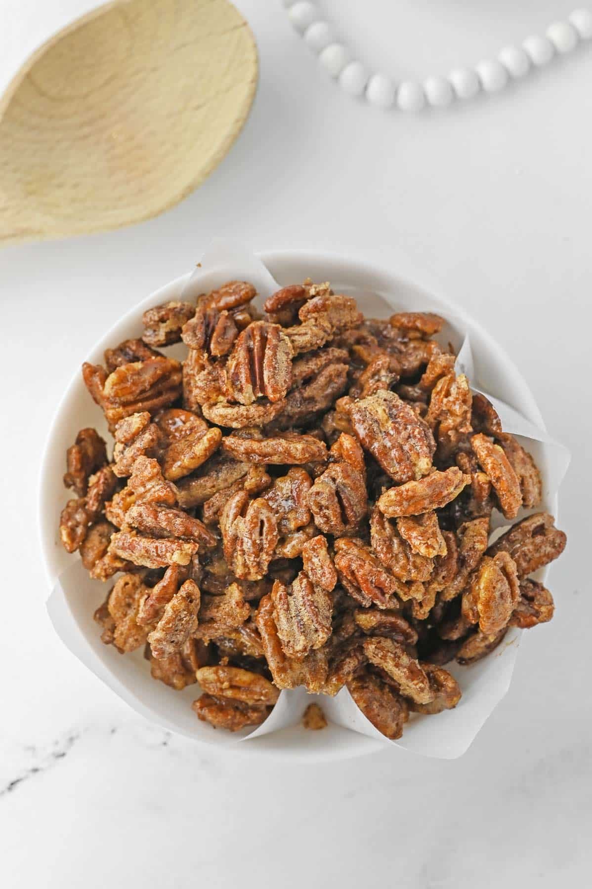 easy candied pecans in a white bowl with a wooden spoon next to it.