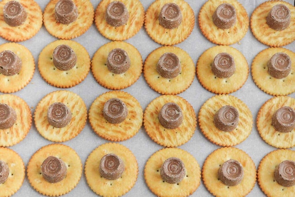 A tray of ritz crackers with rolo caramel candy on each of them.