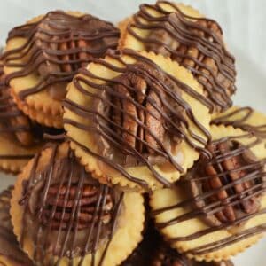 ritz cracker cookies with chocolate drizzle and a pecan half on top.