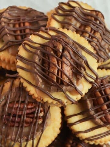 ritz cracker cookies with chocolate drizzle and a pecan half on top.