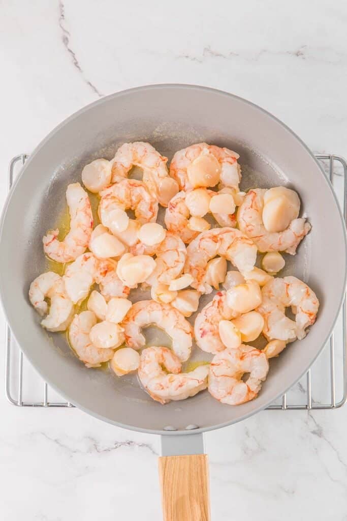 Shrimp and scallops with butter in a large frying pan.
