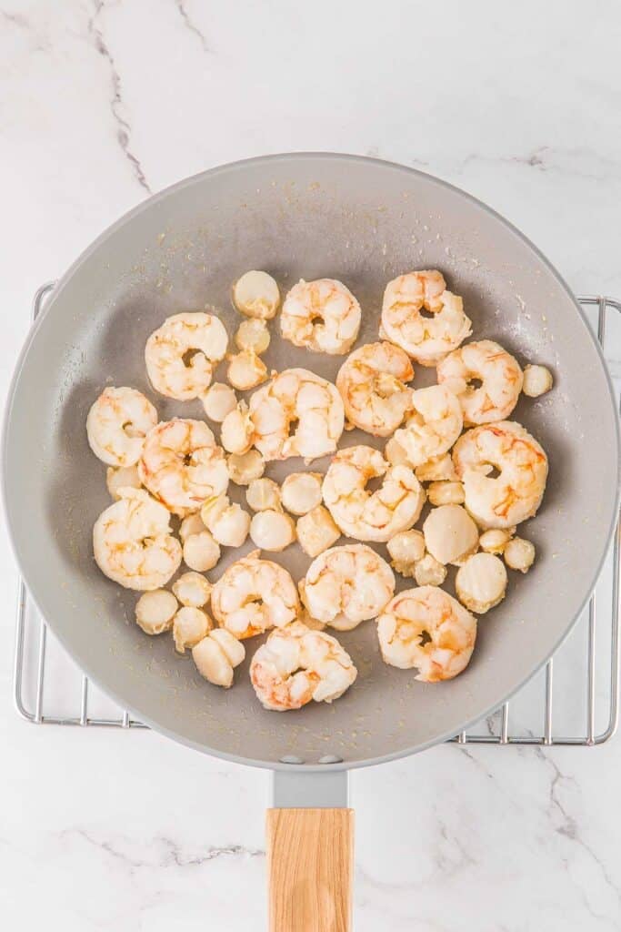 Shrimp and scallops in a large frying pan.