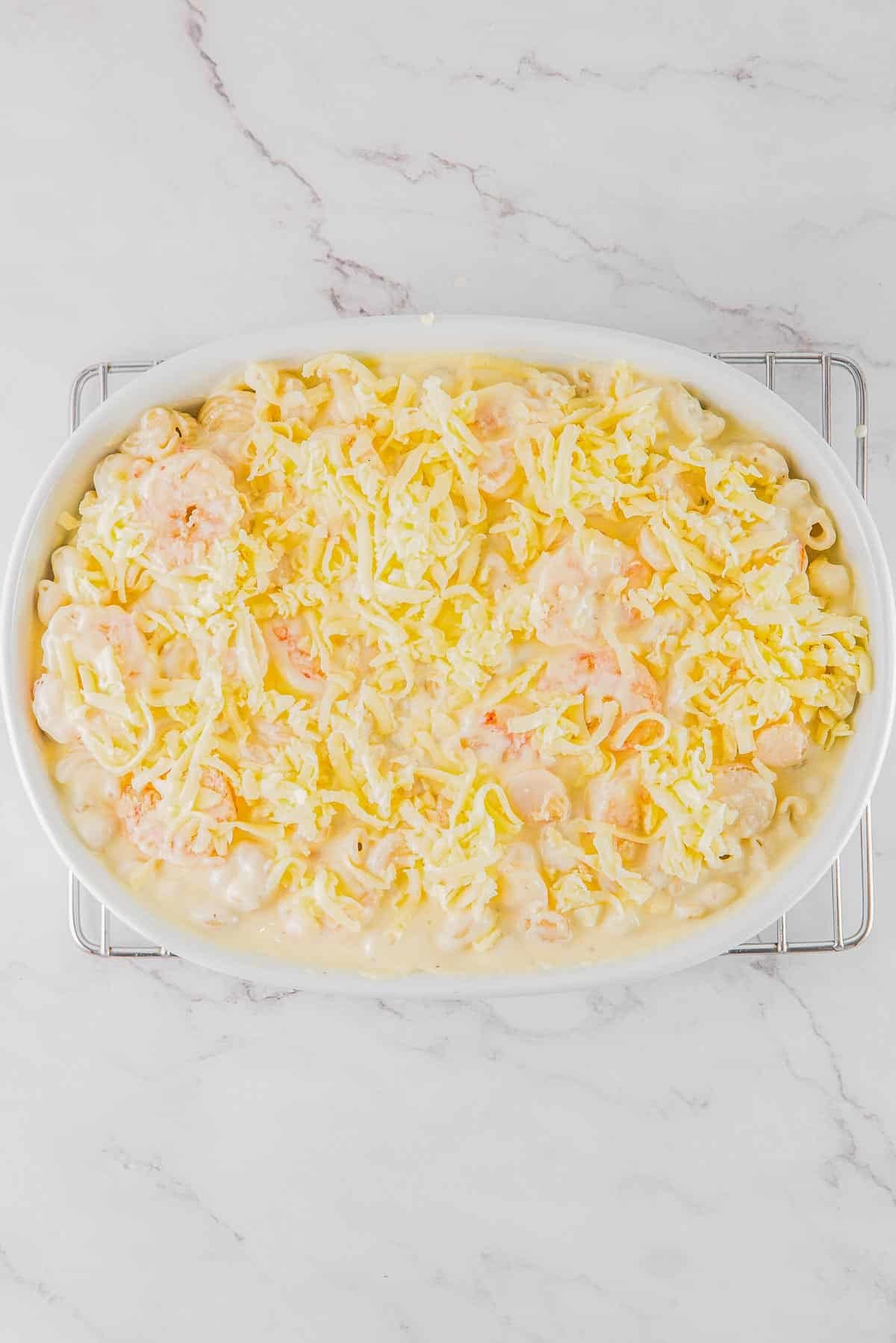 A white dish with shrimp and macaroni in it topped with shredded mozzarella cheese.
