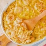 A white dish of seafood macaroni and cheese with a wooden spoon.