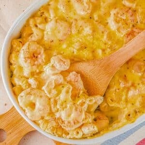 A white dish of seafood macaroni and cheese with a wooden spoon.
