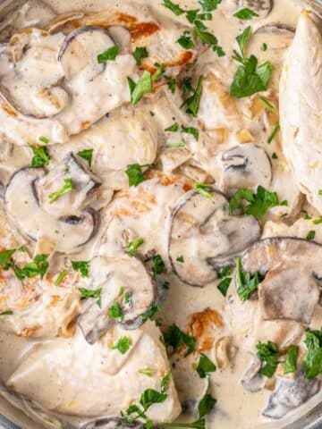 skillet full of creamy chicken with mushroom sauce topped with parsley.