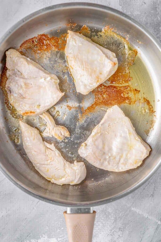 four thin chicken breasts pieces frying in a pan.