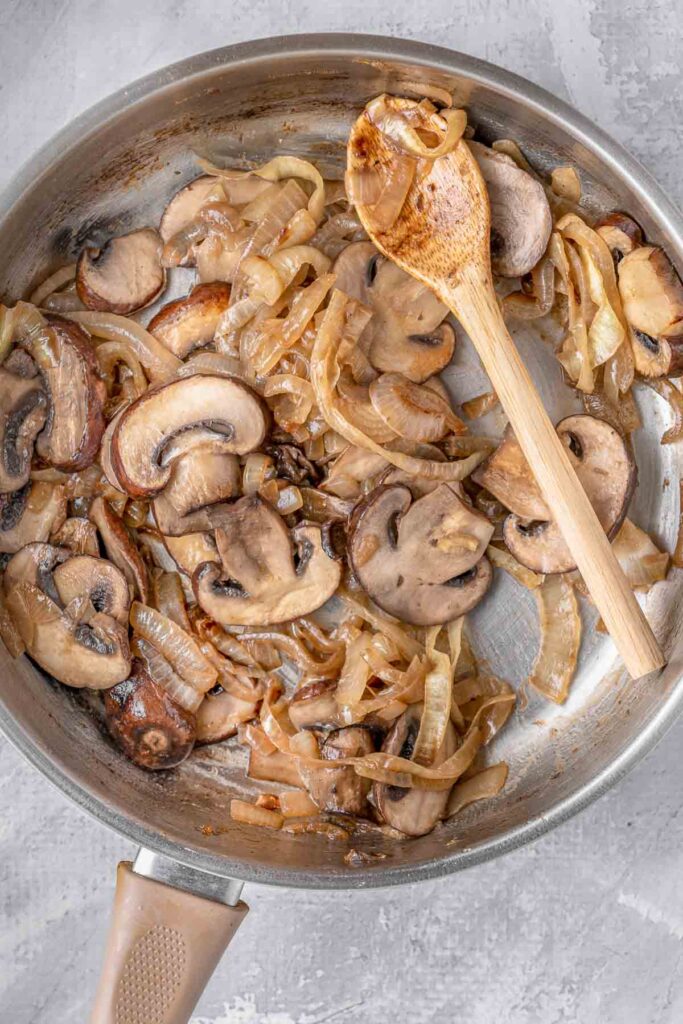 mushrooms and onions in a pan with a wooden spoon.