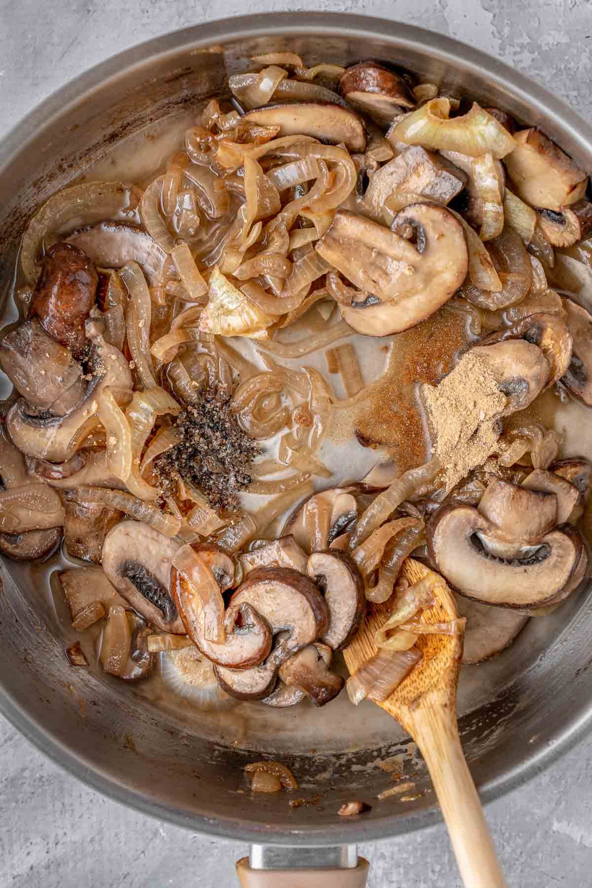 Sautéed mushrooms and onions in a pan with a wooden spoon.