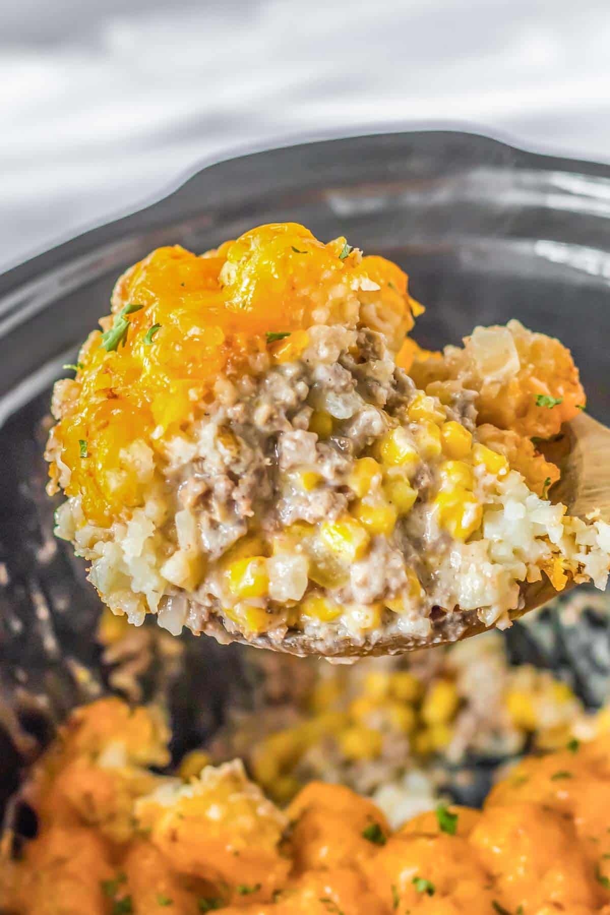 A spoonful of cheesy tater tot casserole in a crock pot.