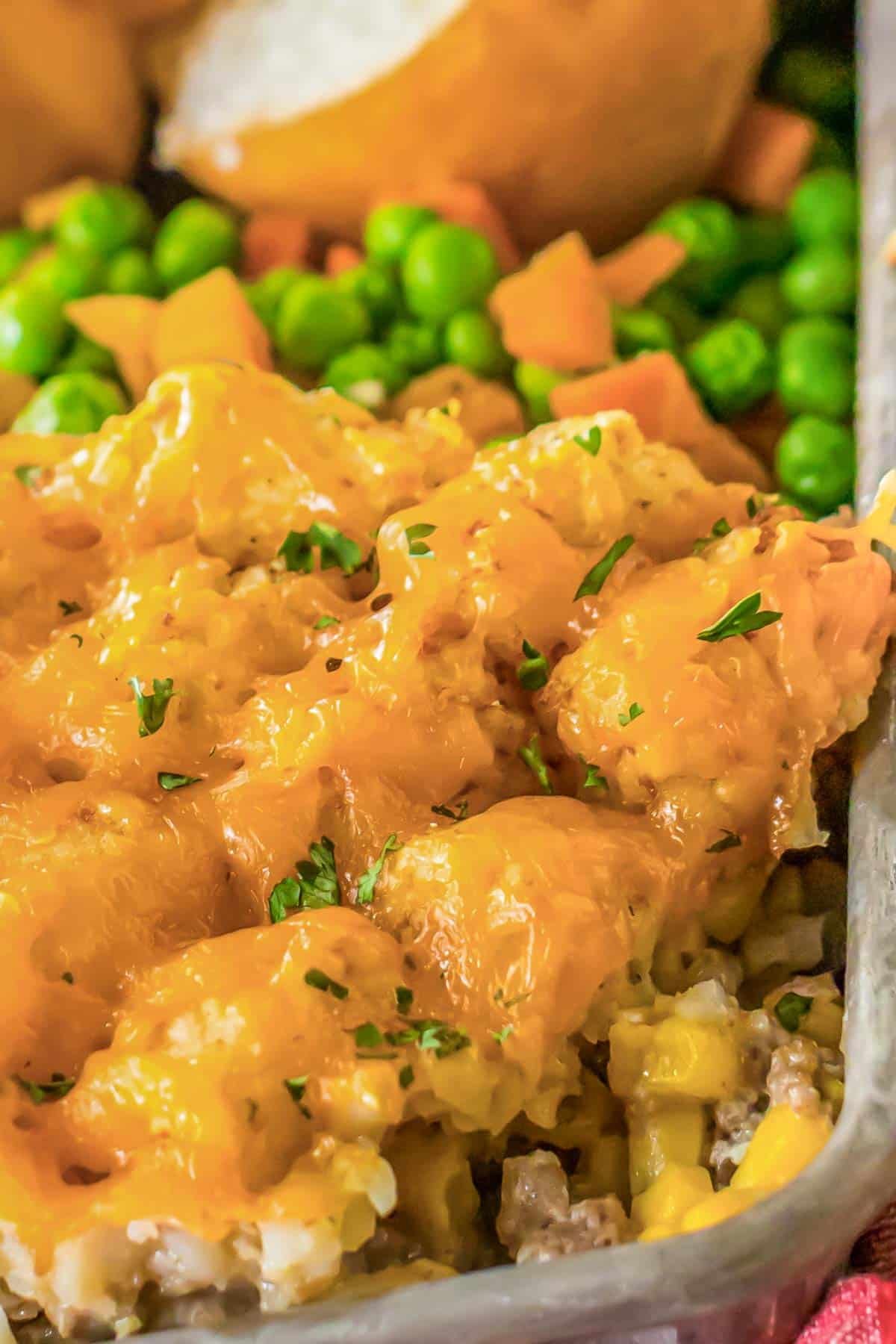 Cheesy tater tot casserole in a baking dish with peas and carrots.