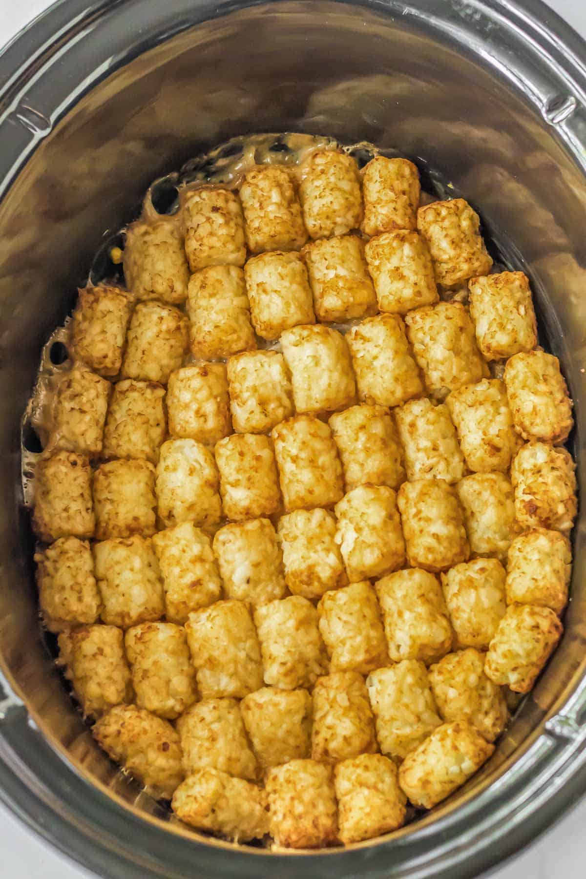 tater tots in a single layer in a black slow cooker.