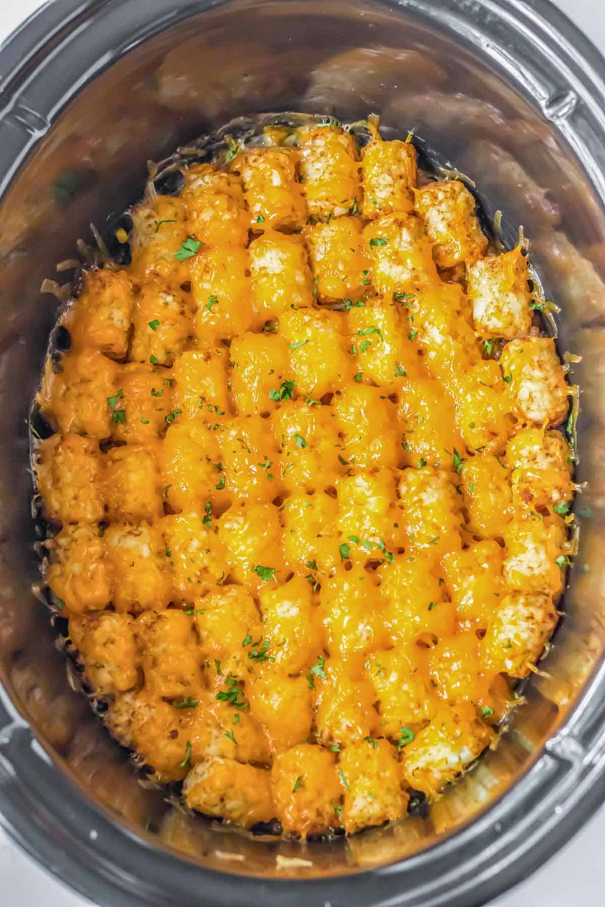A black crock pot filled with cheesy tater tots.
