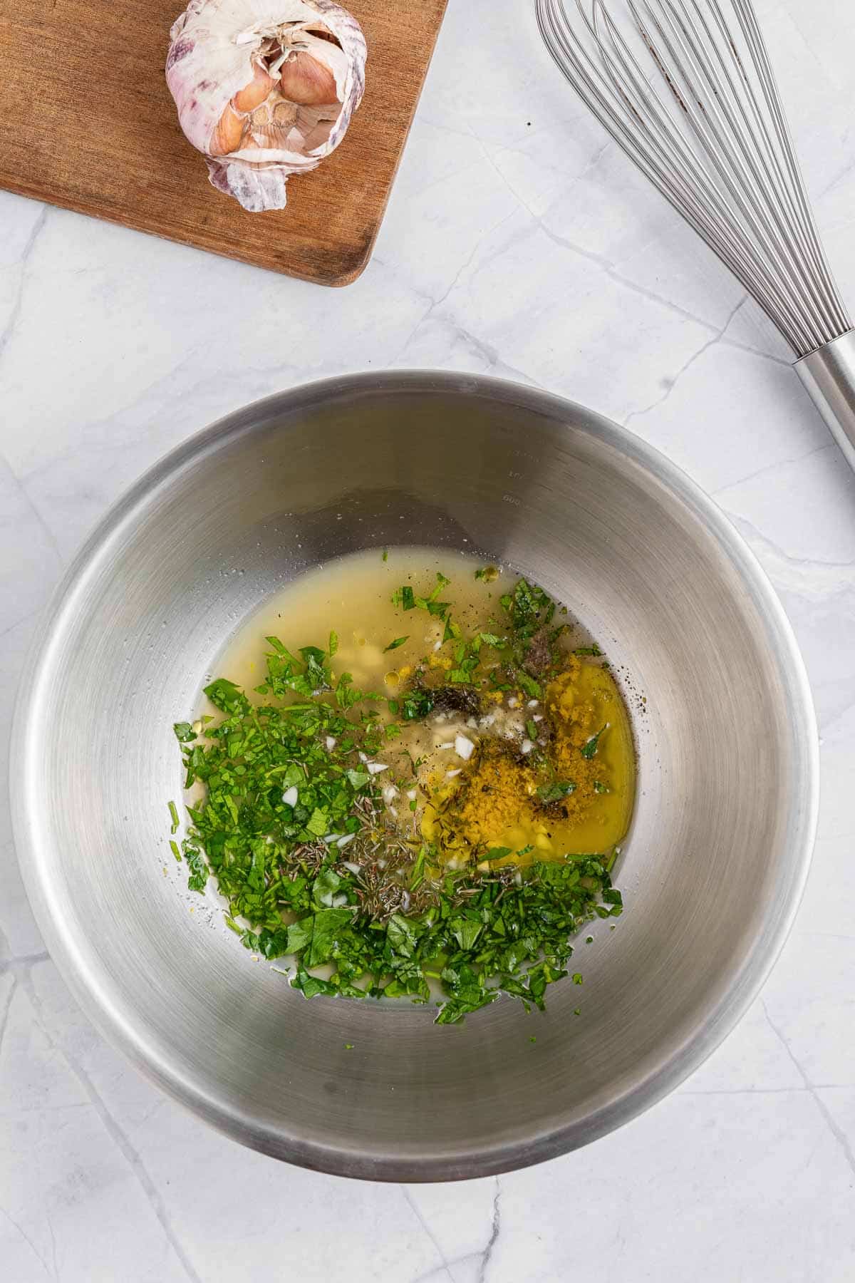 A bowl with garlic, herbs, and a whisk.