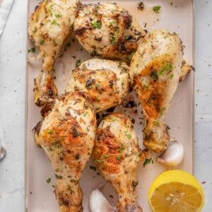 plate full of crispy chicken drumsticks with lemon wedges and garlic cloves.