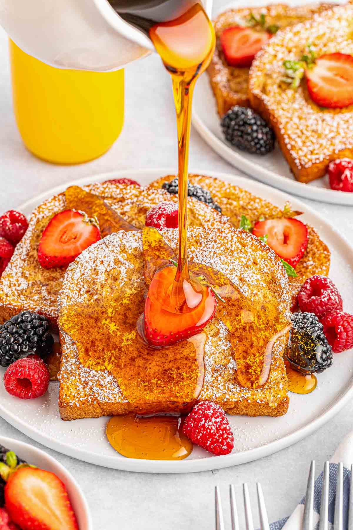 A white plate of air fryer french toast with syrup being poured over it.
