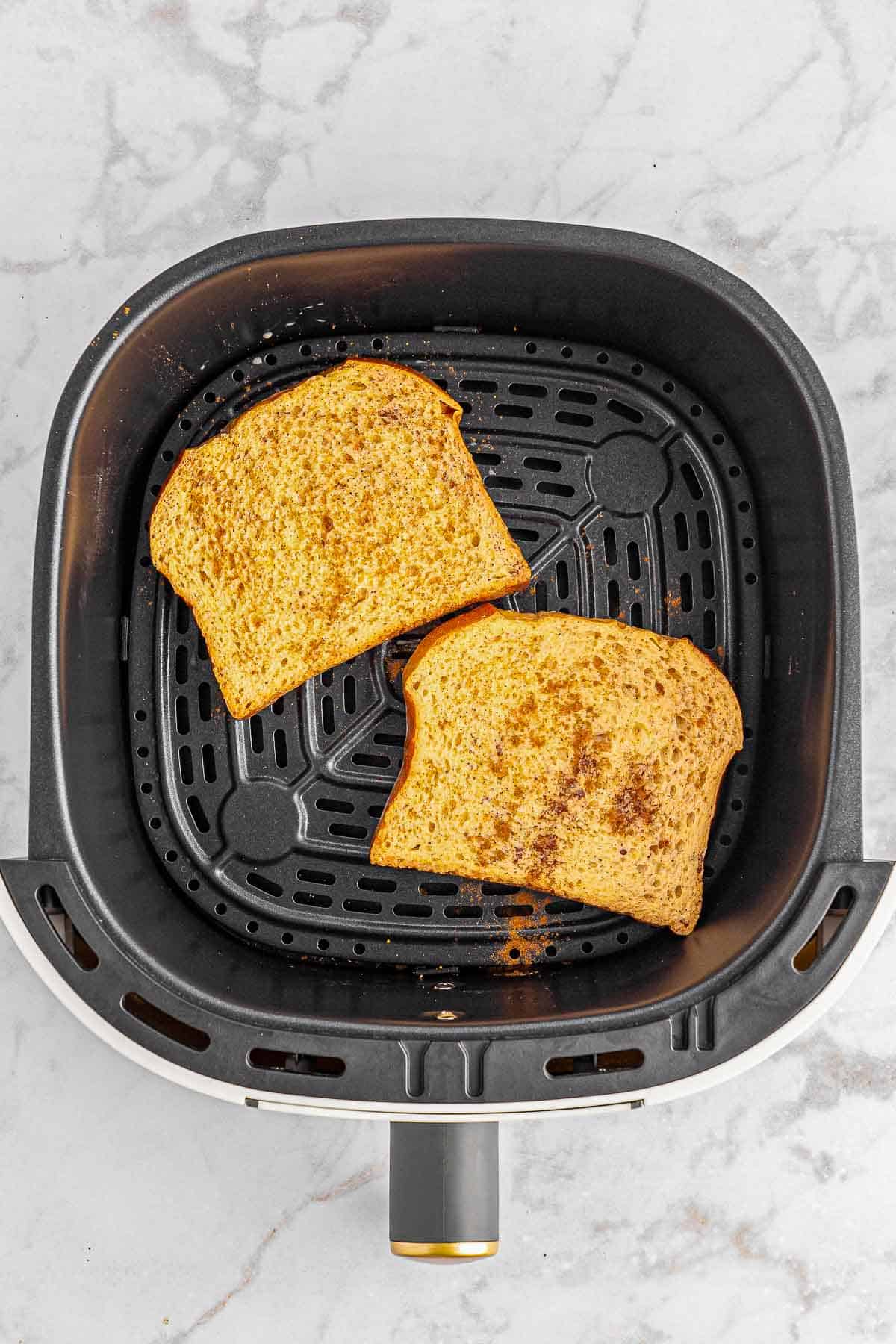 Two slices of egg coated bread in an air fryer.