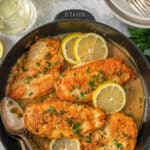 Chicken picata coated in sauce in a skillet topped with lemon and parsley.