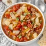 A white bowl full of an easy manhattan clam chowder recipe with bacon, tomatoes and potatoes.