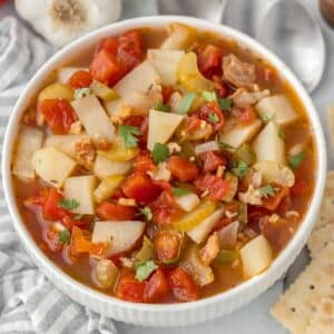 A white bowl full of an easy manhattan clam chowder recipe with bacon, tomatoes and potatoes.