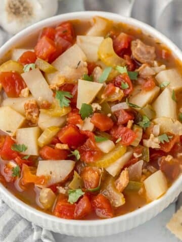 A white bowl full of an easy manhattan clam chowder recipe with bacon, tomatoes and potatoes.