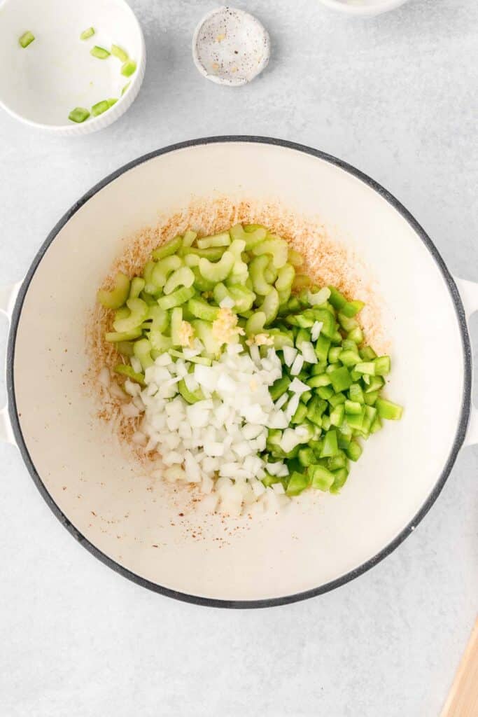 A white pot with diced onions, garlic, celery and green bell peppers.