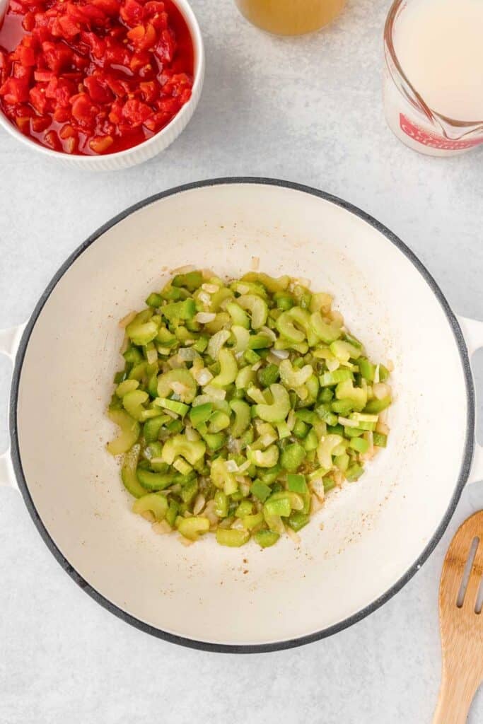 white dutch oven with sautéed celery, green peppers and onions.