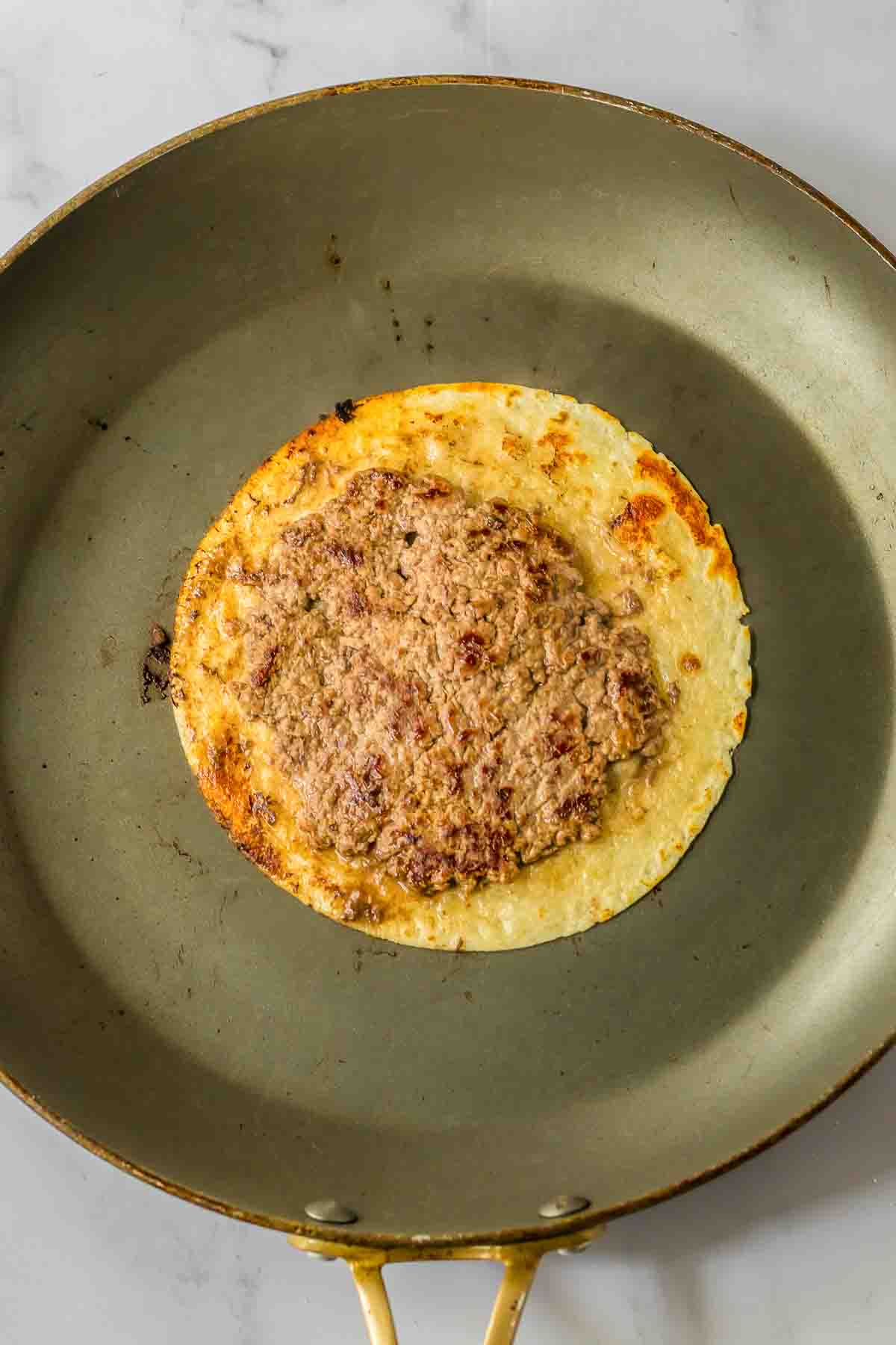 A frying pan cooking a tortilla with ground beef.