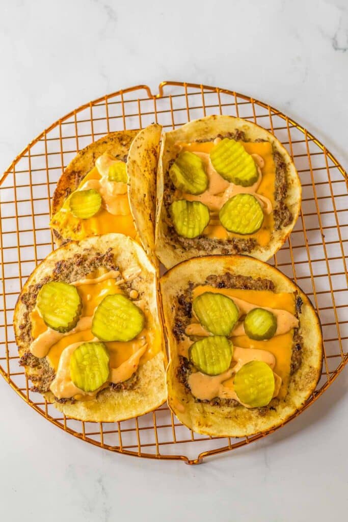 Four tacos with cheese and pickles on a cooling rack.