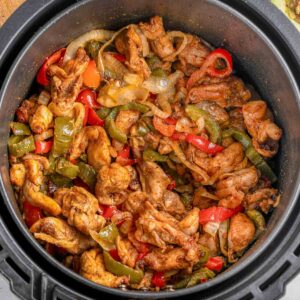 An air fryer basket filled with a chicken fajitas recipe with onions, red and green peppers.