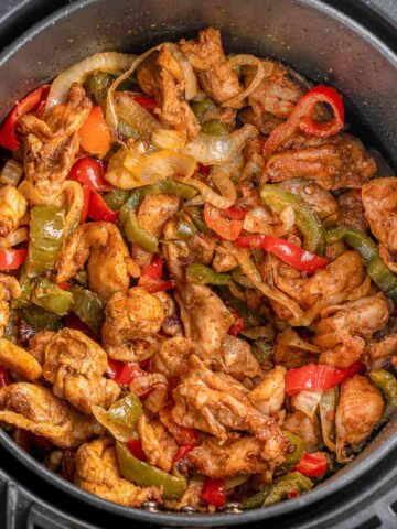 An air fryer basket filled with a chicken fajitas recipe with onions, red and green peppers.