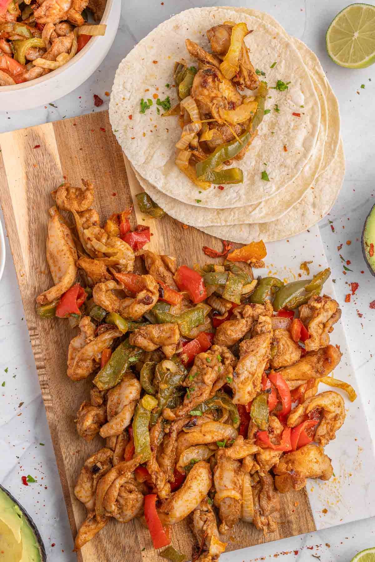 Chicken fajitas on a cutting board with salsa and tortillas.