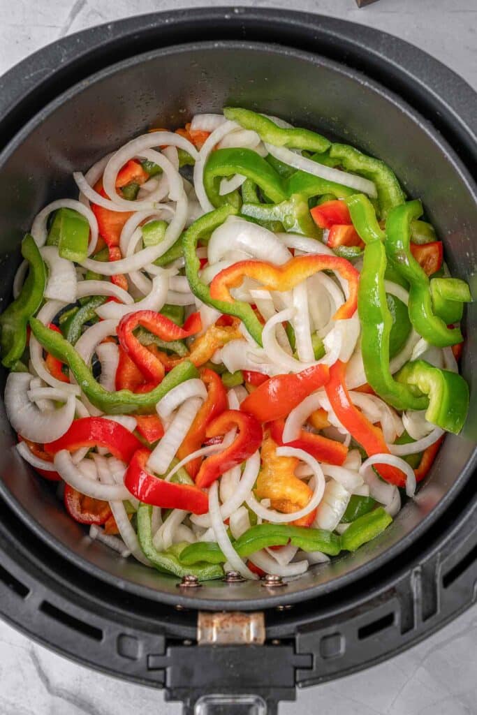 An air fryer filled with sliced onions and red and green peppers.