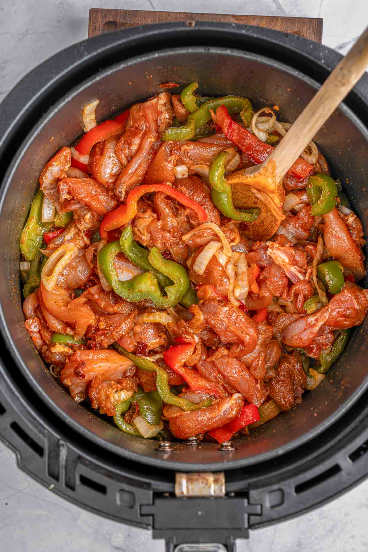 A air fryer filled with raw sliced chicken with onions and peppers.