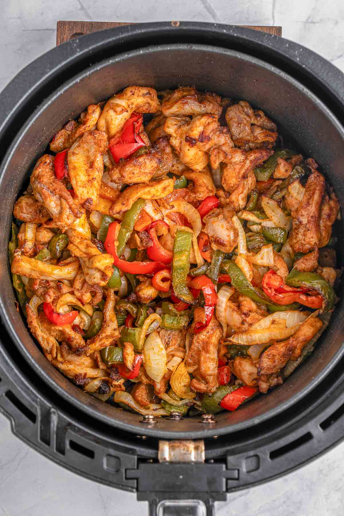 An air fryer filled with chicken fajitas with red and green peppers.