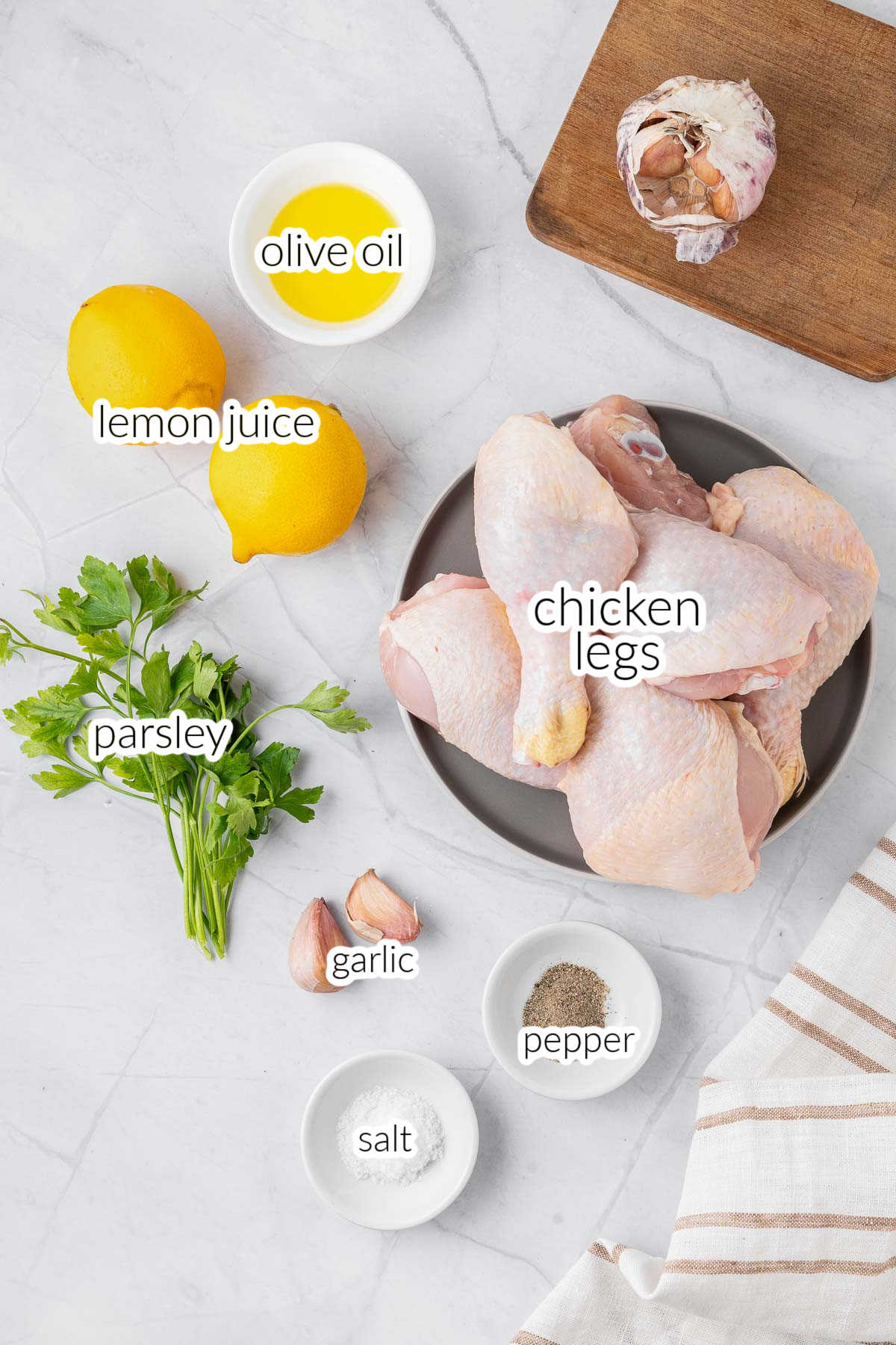 Ingredients for an air fryer chicken legs recipe on a marble counter - raw chicken drumsticks, lemons, garlic, parsley, olive oil salt and pepper.