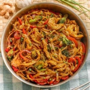 A skillet full of a drunken noodles recipe with rice noodles, chicken and red bell peppers and broccoli.