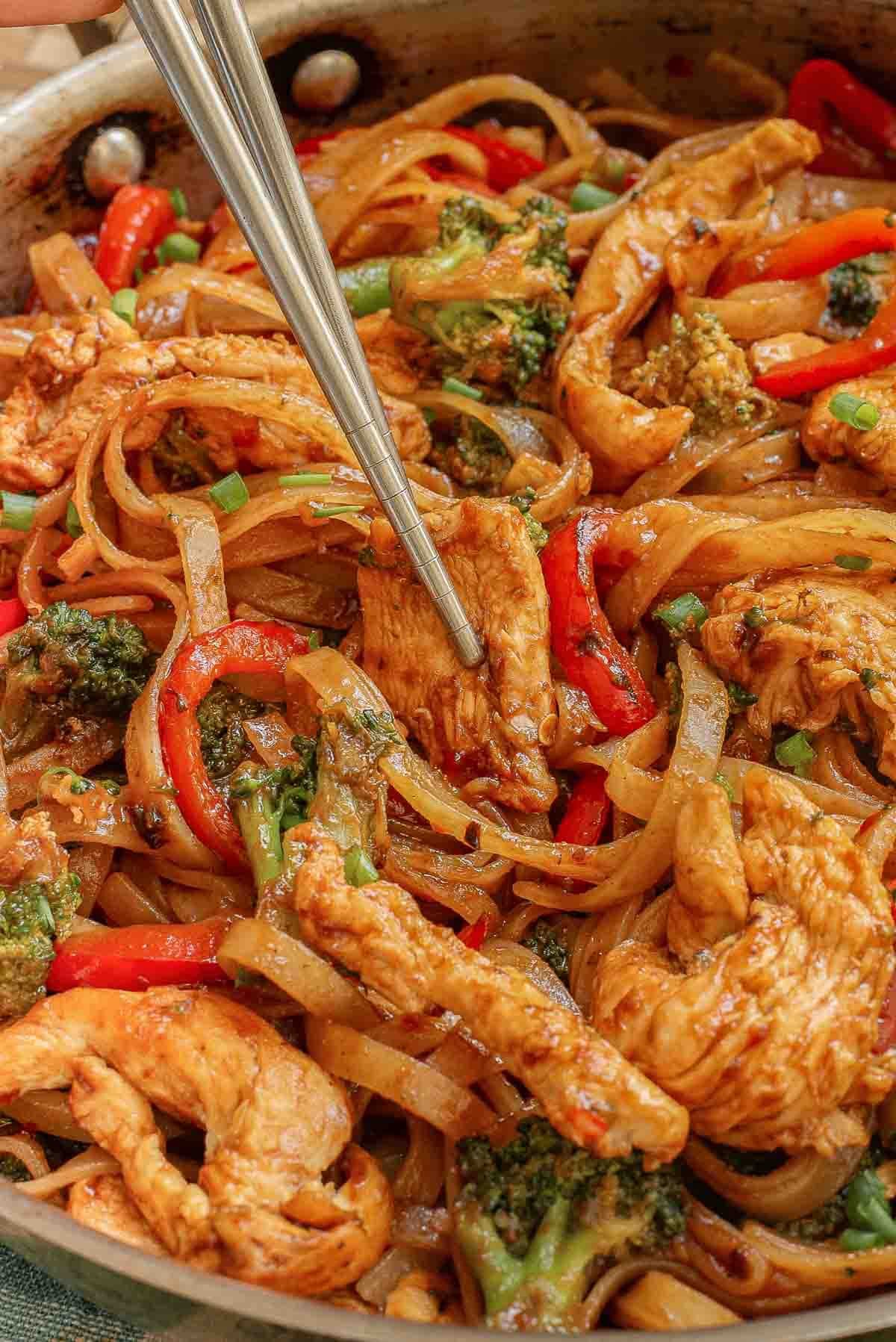 A skillet full of drunken noodles recipe with chicken, broccoli and red peppers.