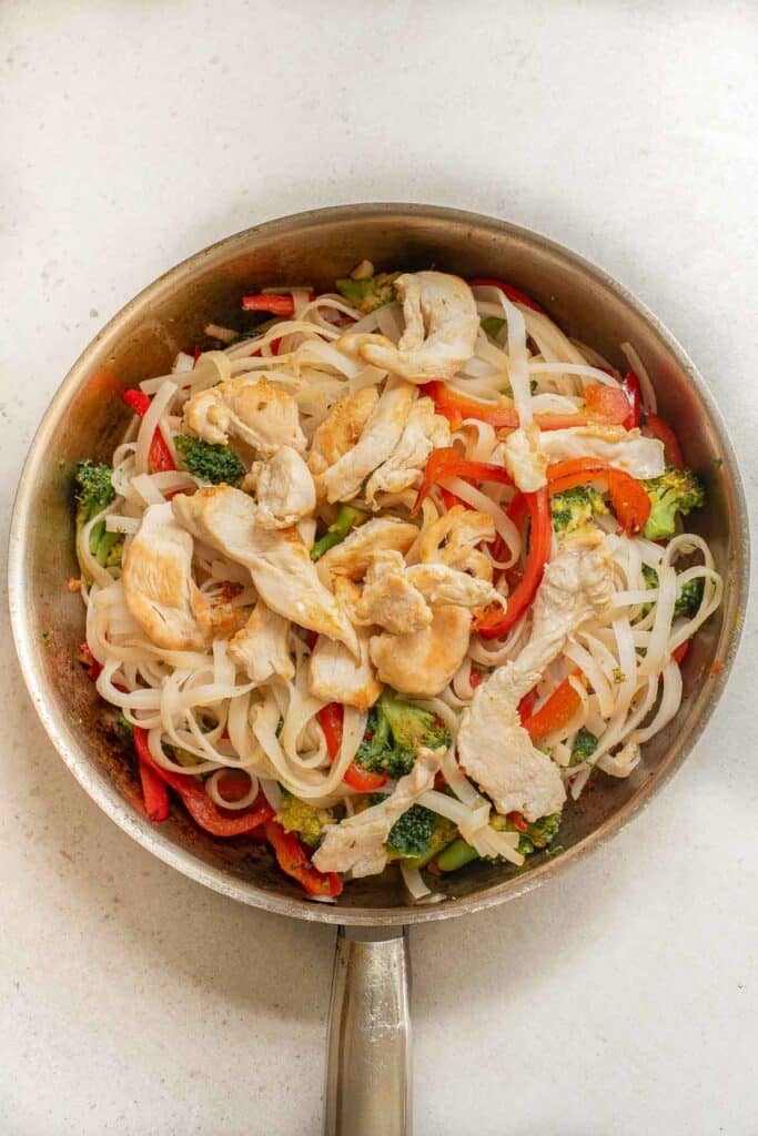 A frying pan filled with noodles, sauteed chicken and vegetables.