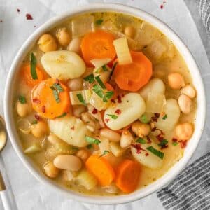 A bowl of gnocchi soup with carrots and beans.