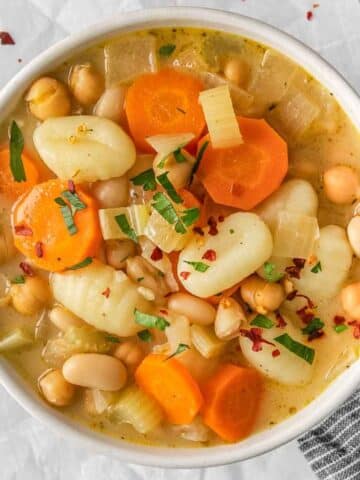 A bowl of gnocchi soup with carrots and beans.