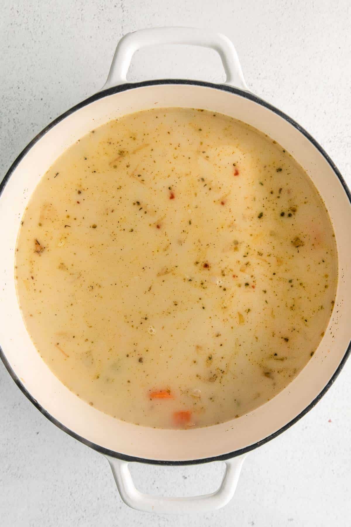 A white pot of soup on a white surface.