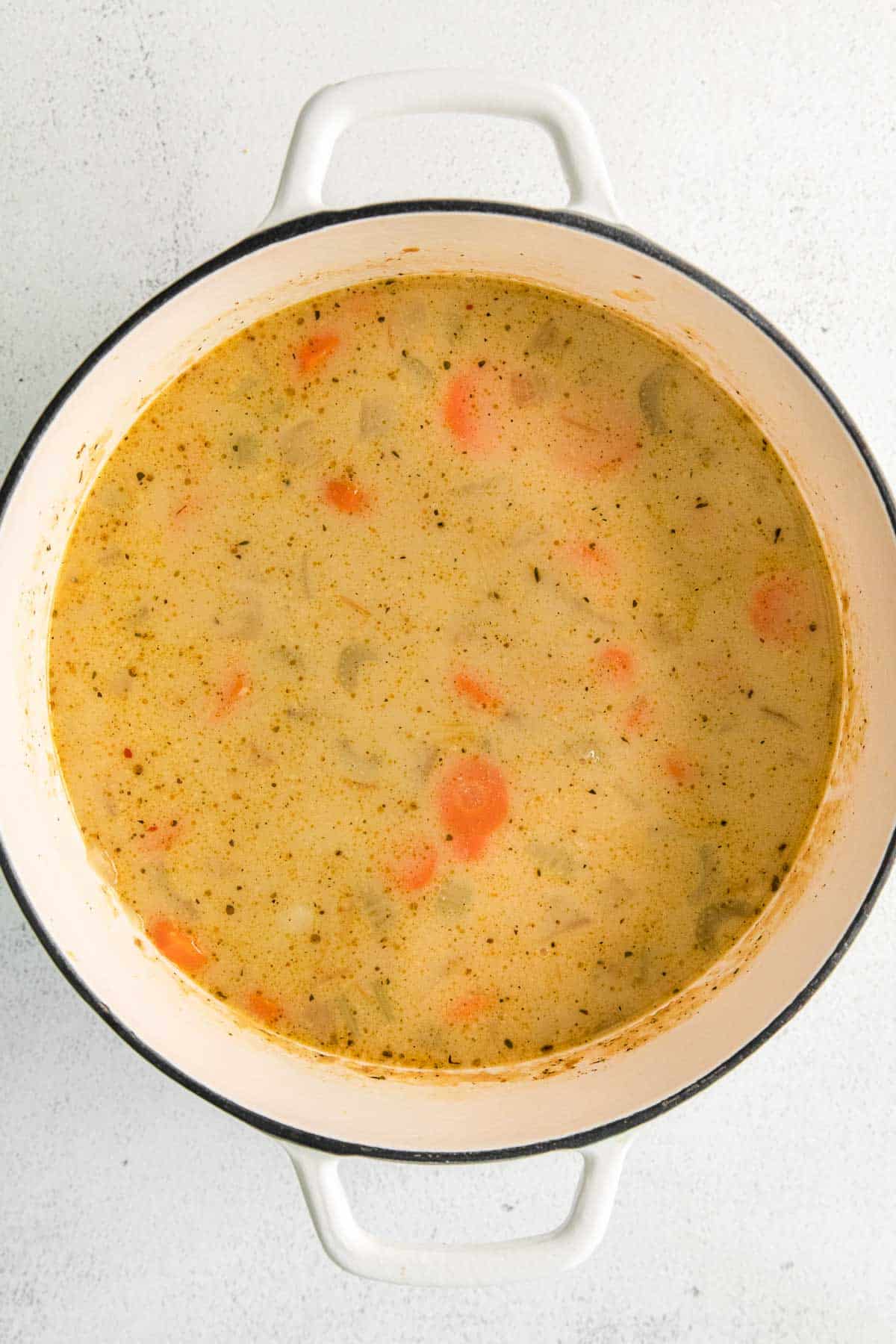 A white pot of soup with carrots and celery in it.