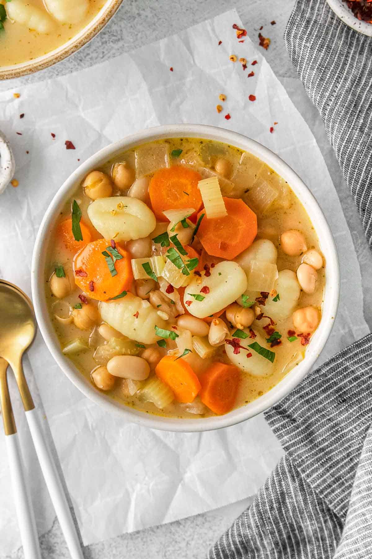 A bowl of gnocchi soup with carrots and white beans.