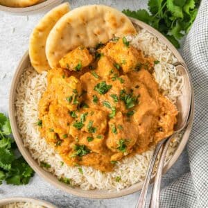 Bowl full of a butter chicken recipe over rice with a spice of naan brea on the side of the bowl.