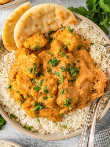 Bowl full of a butter chicken recipe over rice with a spice of naan brea on the side of the bowl.