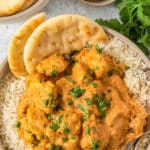 Bowl full of a butter chicken recipe over rice with a spice of naan brea on the side of the bowl.