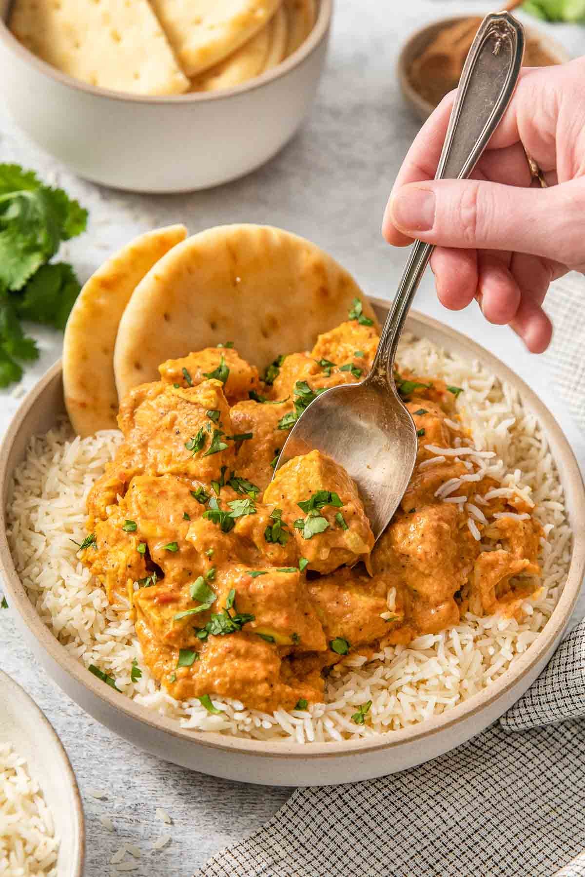 A bowl of a butter chicken recipe over rice with naan bread on the side.