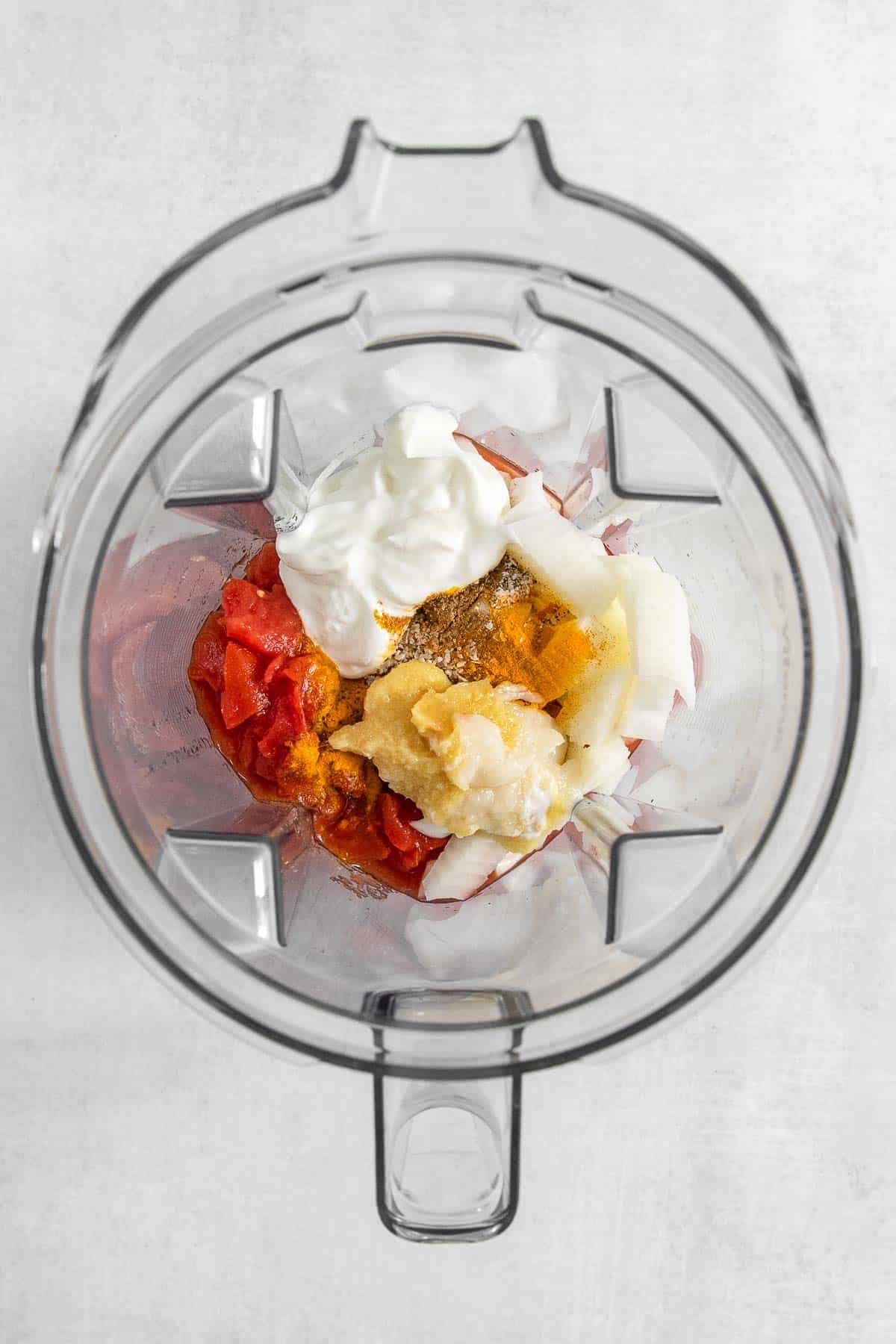 A blender filled with diced tomatoes, yogurt and spices.