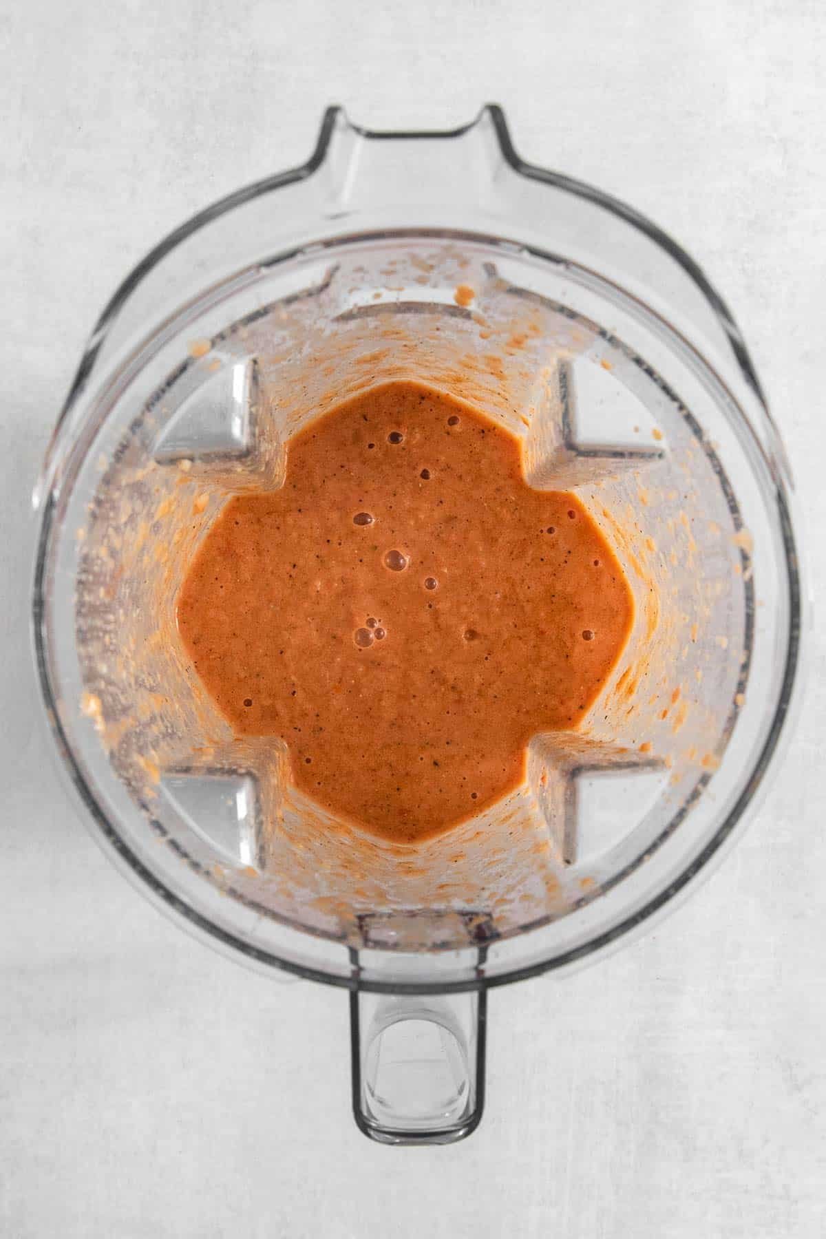 A blender with a creamy red sauce in it.